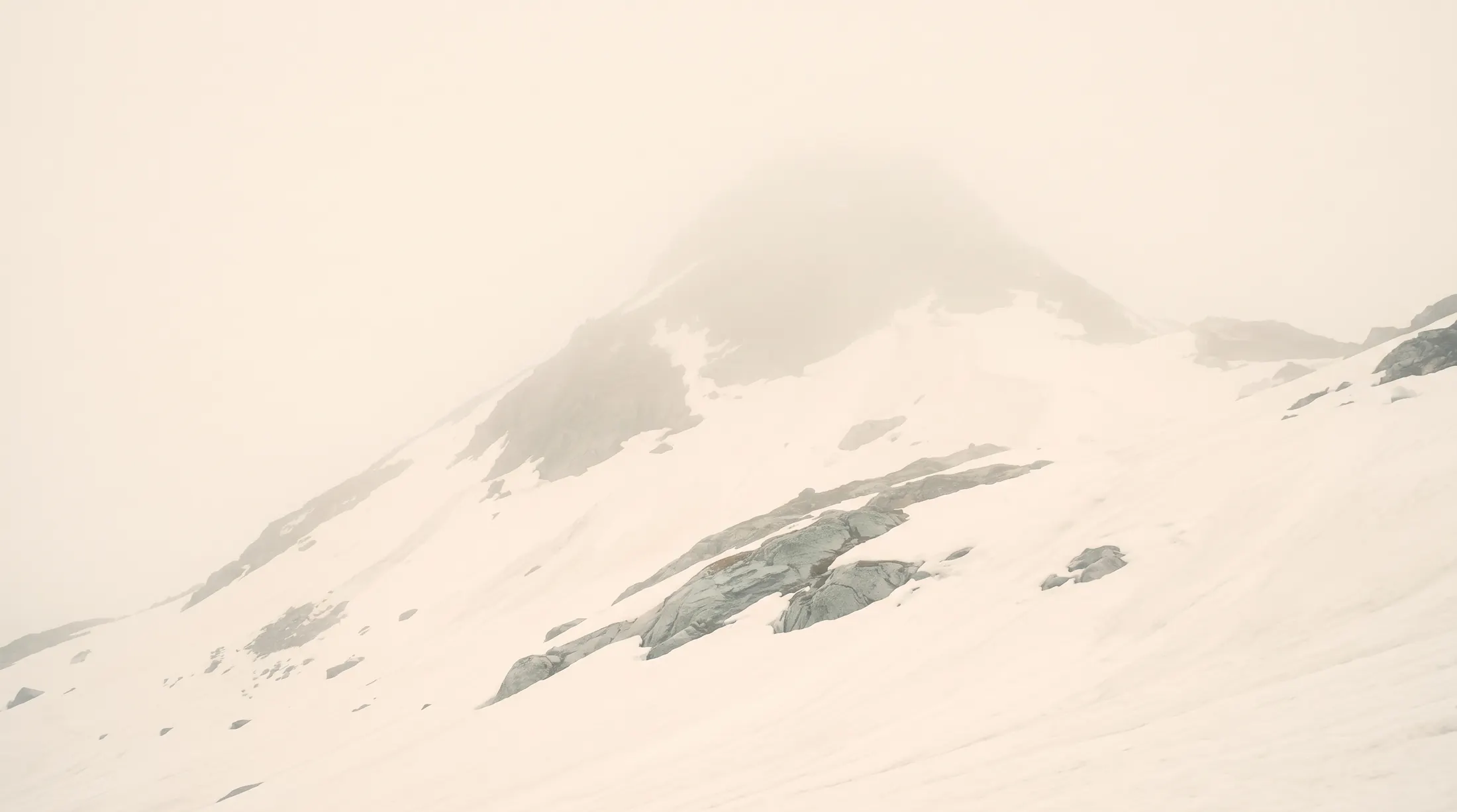 A snow mountain in fog, the ridge line faint against a pale sky.